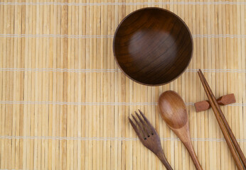 Wooden spoon, chopstick, fork and bowl on bamboo place mat with copy space