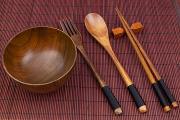 Wooden chopsticks, spoon, fork and bowl on bamboo place mat