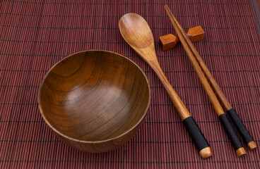 Wooden chopsticks, spoon and bowl on bamboo place mat