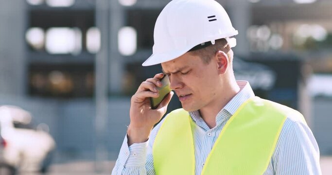Angry foreman quarreling with workers, shouting to cell phone at construction site outdoors, tracking shot