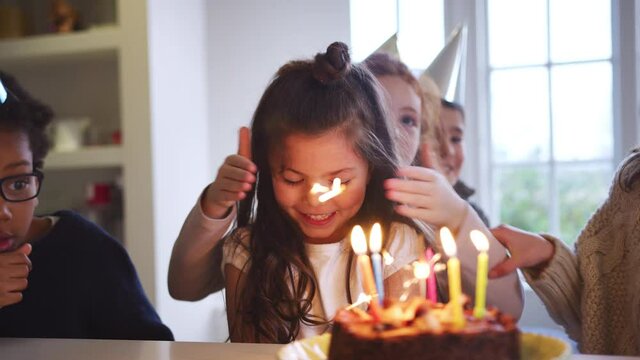 Young girl celebrating birthday with party and group of friends at home being given cake decorated with sparkler and candles - shot in slow motion 