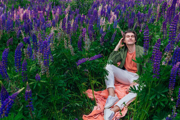 Tall handsome man sitting among the lupine flowers