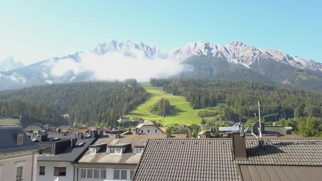 Fly over a Ski Resort Village in the summer with a green ski slope in the background, Innichen, South Tirol, Italy