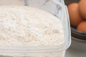 Flour in a plastic bowl close up with some ingredients for baking needs