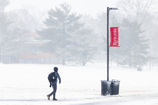 Rutgers University banner in a storm of snow, sleet, and frozen rain; student on campus in foreground.