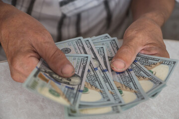 Close-up of an elderly man's hands holding American dollar bills, calculating a home budget. Devaluation concept, selective focus, shallow depth of field