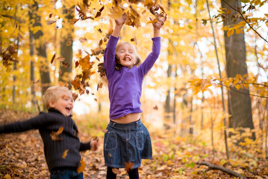 Kids Playing In Yellow Fall Leaves In Autumn