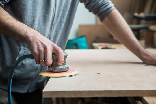 Carpenter using a pneumatic sander to smooth wood