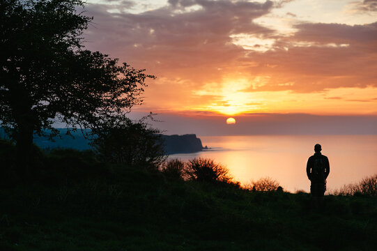 Man standing on cliff watching the sunset over the sea