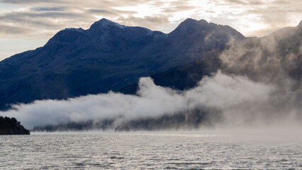 Maloja mountain Pass, Switzerland. Landscape of the lake Sils in the morning during the fall time. The fog covers the lake and the shores. Traditional Swiss contest. Natural landscape