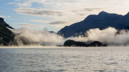 Maloja mountain Pass, Switzerland. Landscape of the lake Sils in the morning during the fall time. The fog covers the lake and the shores. Traditional Swiss contest. Natural landscape