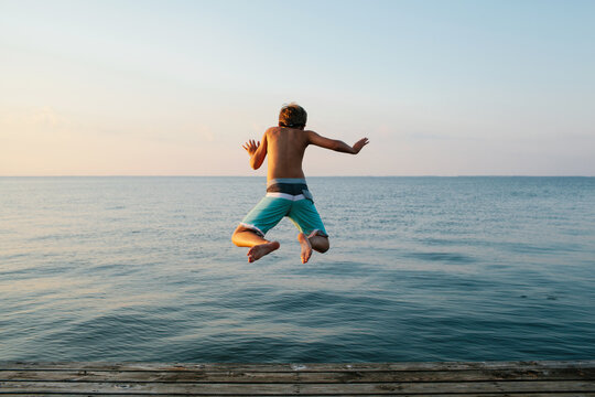 boy jumping off of a pier into a lake at sunset
