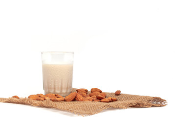 Organic white almond milk in a glass  with whole almonds spilled over a white table. Focus on nutmilk with blurred background.