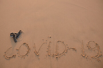 Pandemia of coronavirus. Sign on the sand covid-19 and used medical mascslie next to