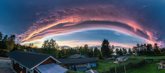 Miraculous panorama of sunset above scandinavian village with rose clouds - edge of cyclone. Arched...