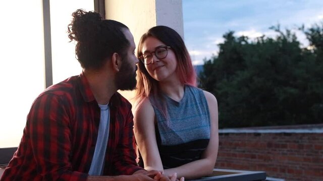 joven pareja mexicana platicando en balcon durante el atardecer relajados sonrientes
