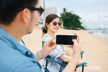 Couple sitting on chair taking photo with smartphone on the beach