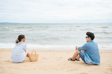 Fototapeta premium Asian couple traveler sitting together on a sand by sea.