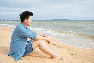 Fototapeta na wymiar Lonely asian man sitting alone looking at the sea on the beach.
