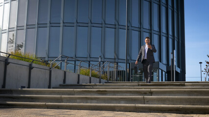 Celebrating success. Low angle view of excited young businessman keeping arms raised and expressing positivity while standing outdoors with office building in the background