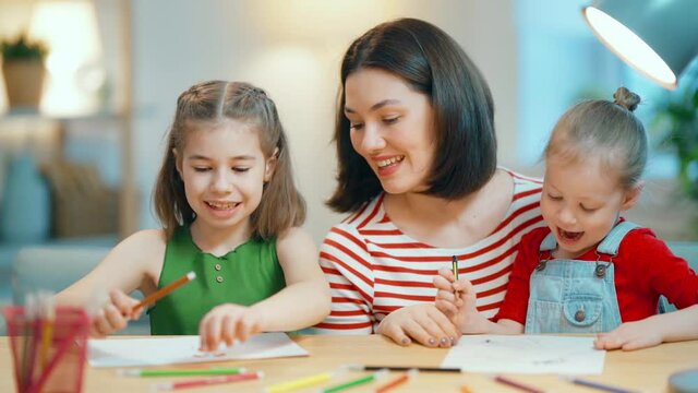 Happy family. Mother and daughters are drawing together. Adult woman helping to child girl.