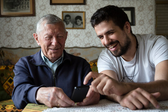 Adult grandson showing to his granddad how to use the phone with touchscreen