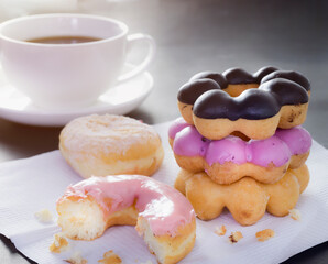 Donuts topped with pink cream that were eaten.  Donuts stacked on top of each other and there is hot coffee behind on dark table