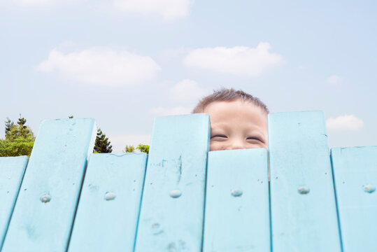 Child smile and hiding himself behide wooden fence