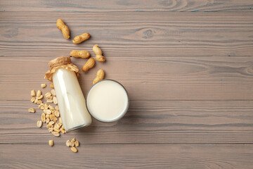 Vegan peanut milk in glass bottle with peanuts on wooden board