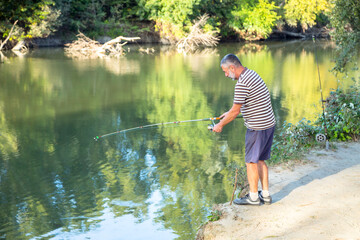 retired man with white beard pulling the rod with old style round reel on the autumn river