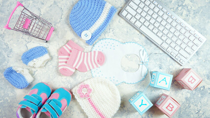 Baby nursery clothing mom bloggers desktop workspace with pink and blue accessories and shopping cart on white marble textured background. Top view blog hero header creative composition flat lay.