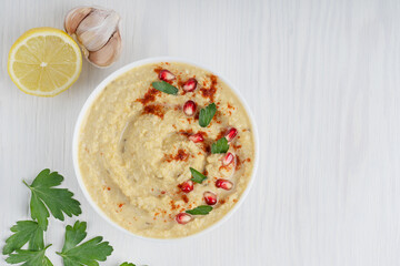 Top view of homemade hummus thick spread made from mashed chickpeas, lemon and garlic used as a dip decorated with pomegranate seeds and parsley on white wooden background. Image with copy space