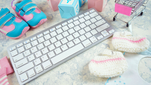 Baby nursery clothing mom bloggers desktop workspace with pink and blue accessories and shopping cart on white marble textured background. Top view blog hero header creative composition flat lay.