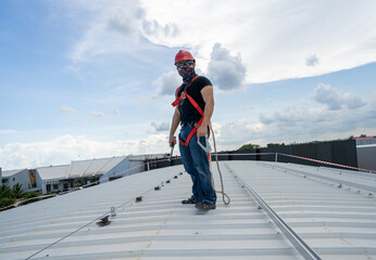 strong look man wear sunglasses red hardhat black shirt blue jeans sneaker and hardness safety belt holding wrench working on metal sheet rooftop in beautiful day stock photo