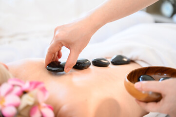 Spa hot stone thai massage beauty treatment.Young woman getting black hot stone on back her in spa salon