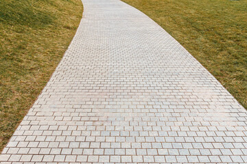 a neat concrete light tile path bends between fresh green grass in a new modern park on a cloudy day