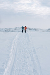 two girls in bright jackets walk along a white snowy road through the tundra beyond the Arctic Circle on a frosty clear day