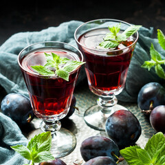 Plum homemade liquor in glasses on dark background with fresh plums