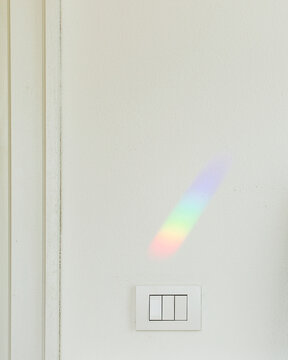 Rainbow shining on wall above light switches