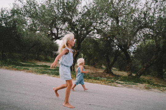 Two little sisters running along the road through olive plantation