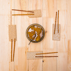 A cup with bee honey, loaves and straws lie on a wooden table
