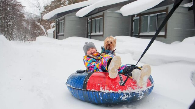father runs along track taking daughter with dog for ride on inflatable sledge in forest on winter day