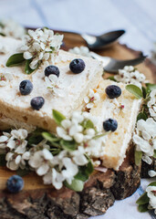 Sweet cake with fresh berries and spring flowers on wood plate,cup of tea, top view 