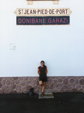 Woman standing against the wall of the train station in Saint-Jean-Pied-de-Port, France