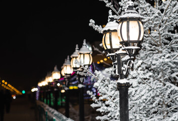 Vintage street lights lit on the streets of the city at night. Winter city landscape. Snow-covered...