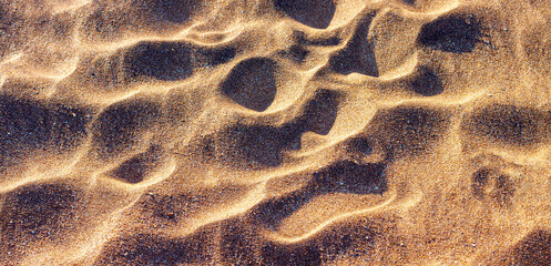 Background of yellow-brown dry sand, illuminated by the setting sun, uneven ripple surface.