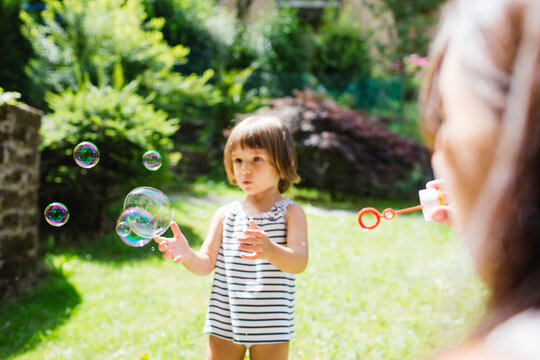 Little girl playing with soap bubbles with her mother
