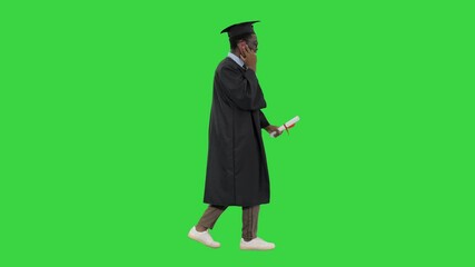 Smiling african american male student in graduation robe talking on the phone while walking on a Green Screen, Chroma Key.
