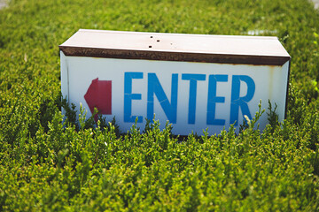 Enter sign with red arrow in shrub / bushes