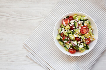 Delicious Avocado Tomato and Cucumber Salad in a bowl on a white wooden background, top view. Flat lay, overhead, from above. Copy space.